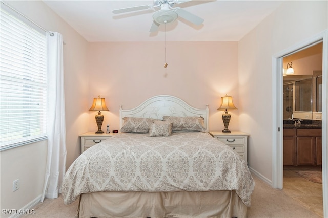 bedroom featuring ceiling fan, ensuite bath, sink, and light colored carpet