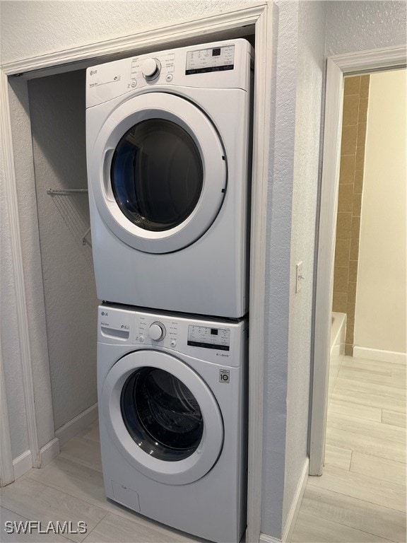 clothes washing area with light hardwood / wood-style floors and stacked washer and clothes dryer