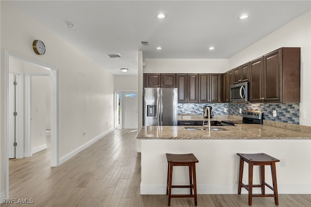 kitchen with dark brown cabinetry, a peninsula, a sink, appliances with stainless steel finishes, and light stone countertops