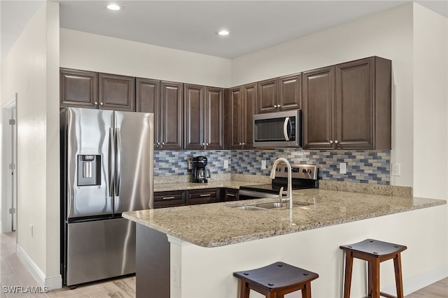 kitchen featuring light stone counters, a breakfast bar area, appliances with stainless steel finishes, dark brown cabinetry, and a peninsula