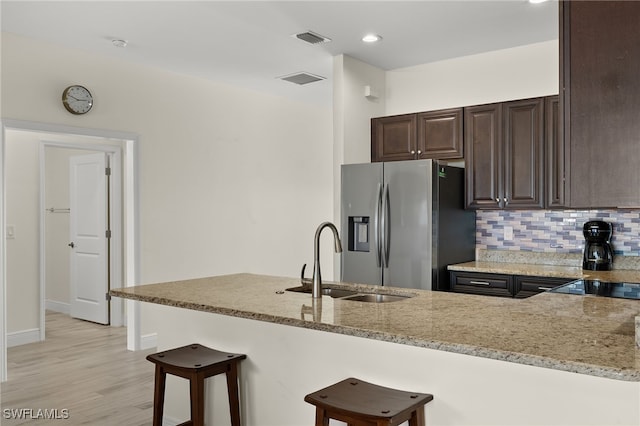 kitchen featuring a breakfast bar, visible vents, a sink, light stone countertops, and stainless steel fridge