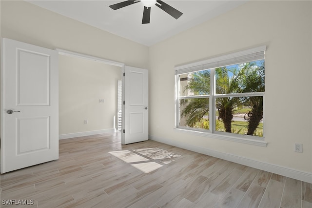 spare room featuring ceiling fan, light wood-style flooring, and baseboards