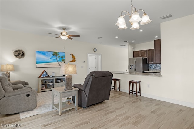 living area featuring visible vents, ceiling fan with notable chandelier, light wood-style flooring, and baseboards