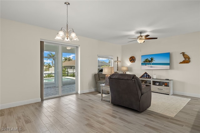 living area featuring baseboards, light wood finished floors, and ceiling fan with notable chandelier