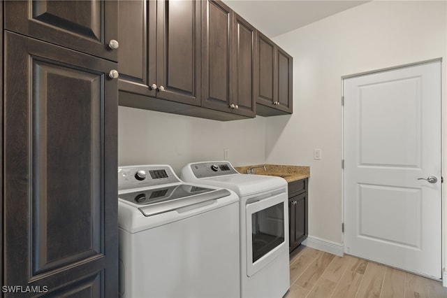 laundry room featuring a sink, baseboards, light wood-style floors, cabinet space, and washing machine and clothes dryer