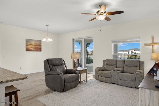 living area with ceiling fan with notable chandelier, light wood-type flooring, and baseboards