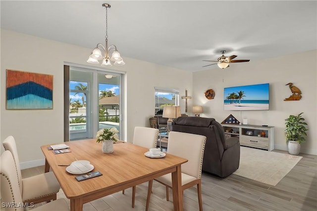 dining area with light wood-style floors, baseboards, and ceiling fan with notable chandelier