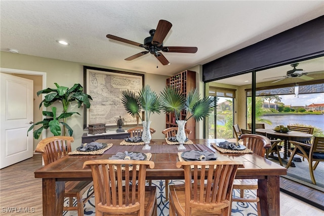 dining room featuring a water view, ceiling fan, a textured ceiling, and light hardwood / wood-style floors