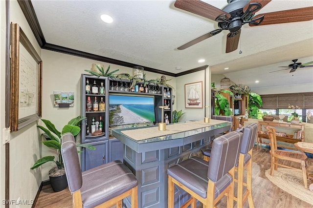 bar with crown molding, a textured ceiling, light wood-type flooring, and ceiling fan