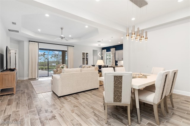 dining room with a tray ceiling, ceiling fan, and light hardwood / wood-style floors