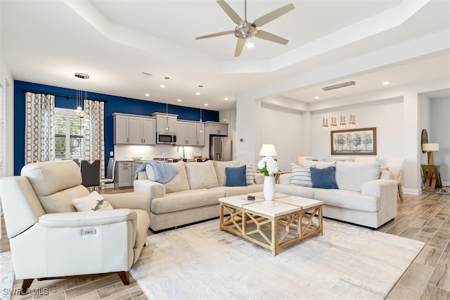 living room with a tray ceiling, ceiling fan, and light hardwood / wood-style floors