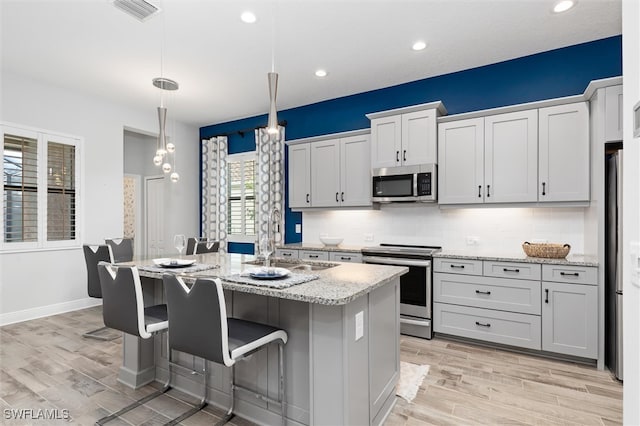 kitchen featuring light hardwood / wood-style floors, light stone countertops, stainless steel appliances, and a kitchen island with sink