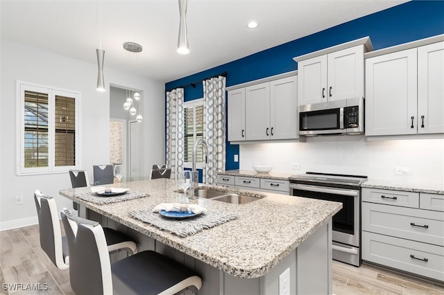 kitchen featuring sink, a kitchen breakfast bar, light hardwood / wood-style flooring, decorative light fixtures, and appliances with stainless steel finishes