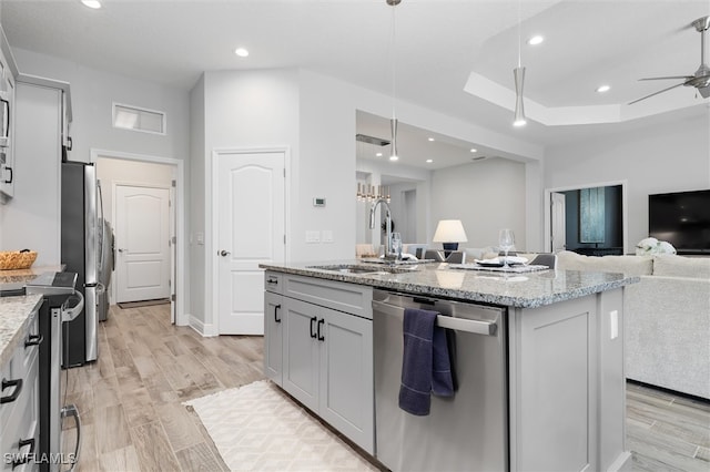 kitchen featuring light stone counters, stainless steel appliances, sink, pendant lighting, and an island with sink