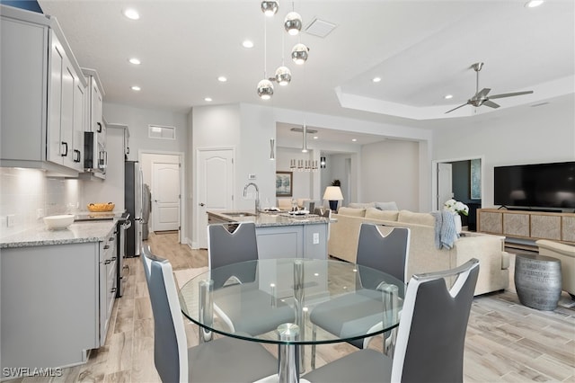 dining area featuring ceiling fan with notable chandelier, light hardwood / wood-style floors, and sink