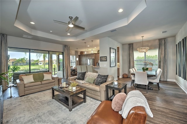 living room with hardwood / wood-style flooring, a tray ceiling, and ceiling fan with notable chandelier