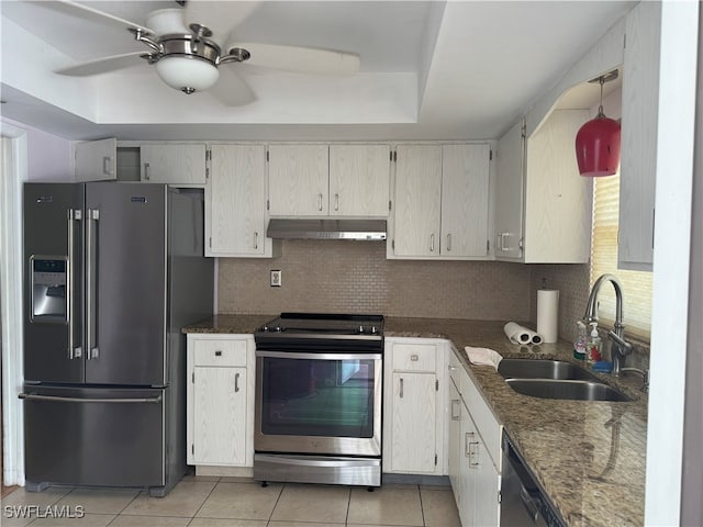 kitchen with dark stone counters, sink, light tile patterned floors, a tray ceiling, and stainless steel appliances