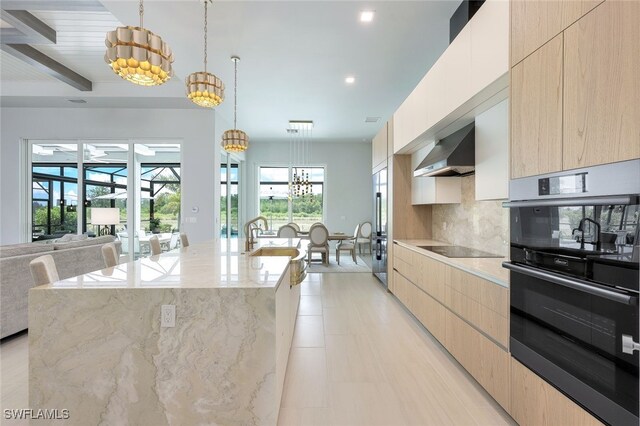 kitchen featuring pendant lighting, decorative backsplash, wall chimney exhaust hood, black appliances, and a spacious island