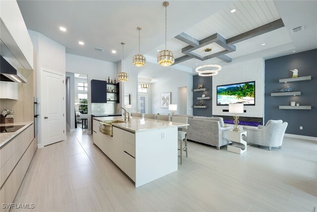 kitchen featuring a large island with sink, sink, light stone countertops, decorative light fixtures, and white cabinets