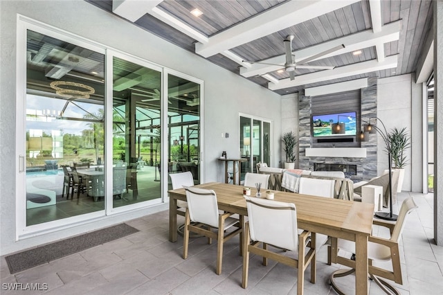 sunroom with a stone fireplace, beamed ceiling, wood ceiling, and ceiling fan