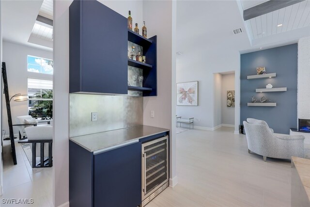 kitchen featuring wine cooler, blue cabinetry, light tile patterned floors, and a towering ceiling