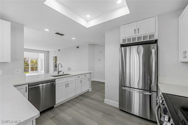 kitchen featuring light wood-type flooring, stainless steel appliances, a tray ceiling, sink, and white cabinets