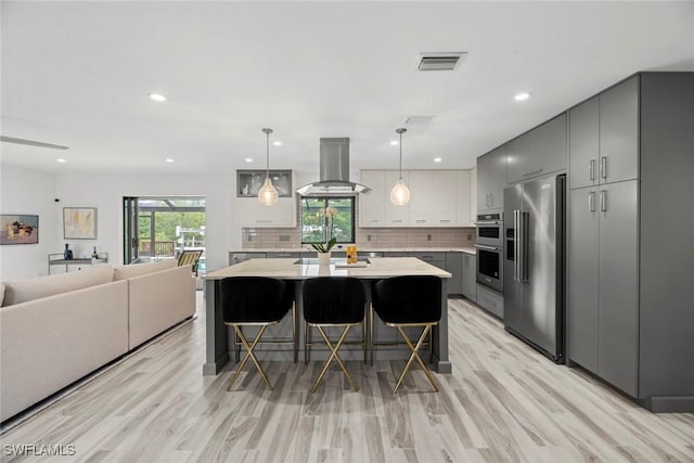 kitchen with appliances with stainless steel finishes, island range hood, a kitchen bar, and gray cabinetry