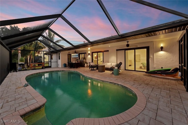 pool at dusk with a lanai, an outdoor hangout area, ceiling fan, and a patio area