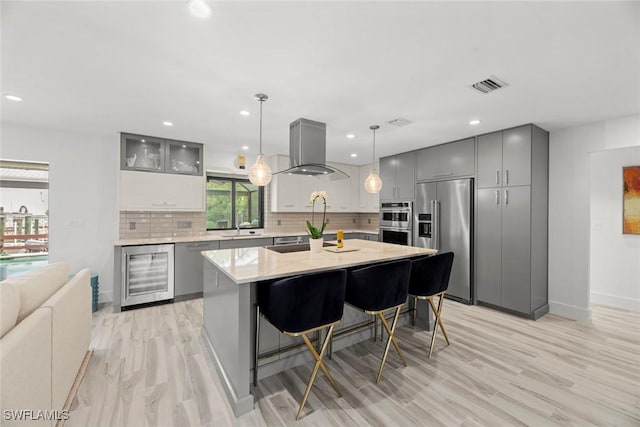 kitchen with appliances with stainless steel finishes, beverage cooler, backsplash, a center island, and wall chimney range hood