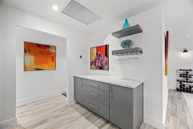 bar featuring light stone countertops, gray cabinetry, and light hardwood / wood-style floors