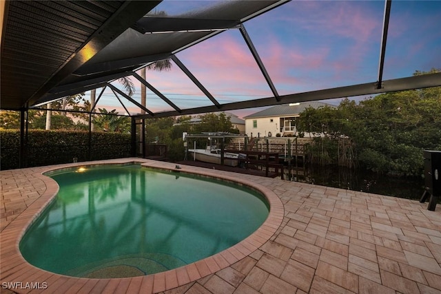 pool at dusk featuring glass enclosure and a patio area