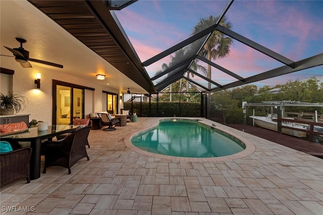 pool at dusk with ceiling fan, an outdoor living space, a lanai, and a patio