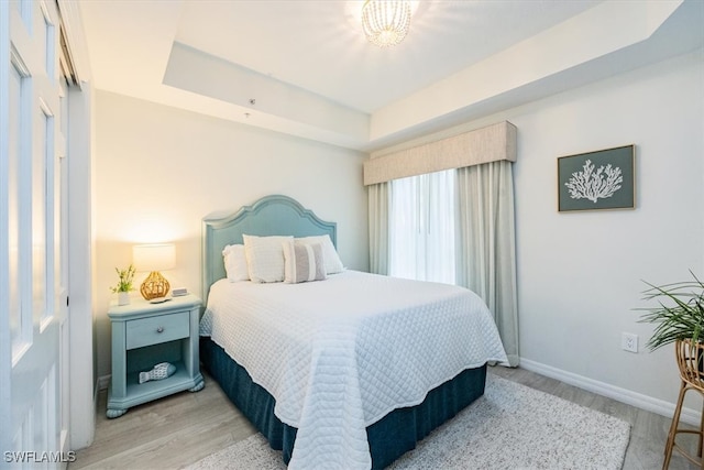 bedroom featuring a tray ceiling and light hardwood / wood-style flooring