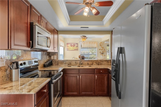 kitchen featuring stainless steel appliances, light stone counters, decorative backsplash, sink, and a tray ceiling