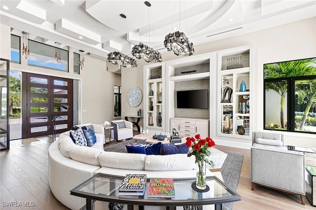 living room featuring plenty of natural light, a towering ceiling, french doors, and light wood-type flooring