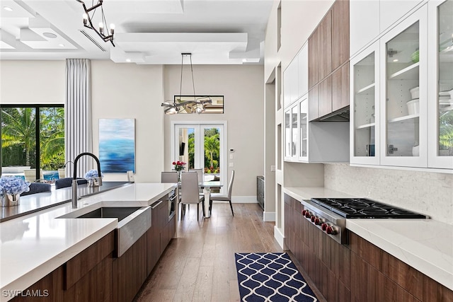 kitchen featuring sink, hanging light fixtures, stainless steel gas stovetop, white cabinets, and light wood-type flooring