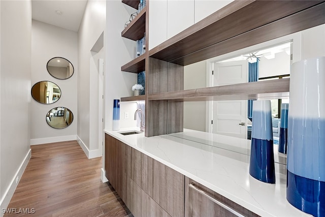 kitchen with white cabinetry, sink, ceiling fan, light stone counters, and light hardwood / wood-style floors