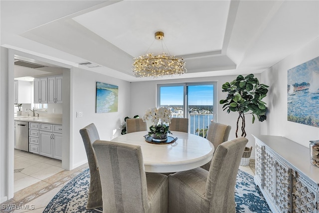 dining room featuring a tray ceiling, sink, light tile patterned floors, a water view, and a notable chandelier