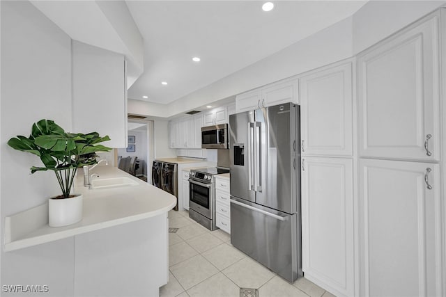 kitchen featuring stainless steel appliances, sink, light tile patterned floors, white cabinets, and washer / dryer