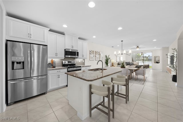 kitchen with white cabinets, stainless steel appliances, sink, a center island with sink, and stone counters