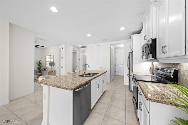 kitchen featuring light stone counters, a center island with sink, white cabinets, and stainless steel appliances