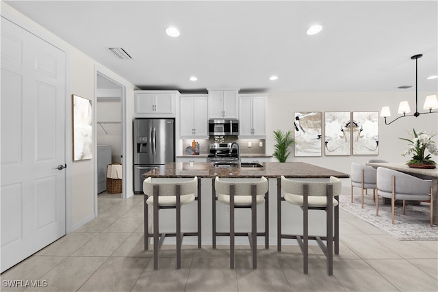 kitchen with sink, dark stone countertops, a kitchen island with sink, white cabinets, and appliances with stainless steel finishes