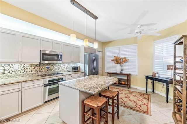 kitchen featuring light stone counters, a kitchen bar, pendant lighting, and appliances with stainless steel finishes