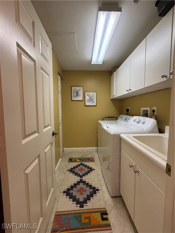 clothes washing area featuring light tile patterned floors, washing machine and dryer, and cabinets