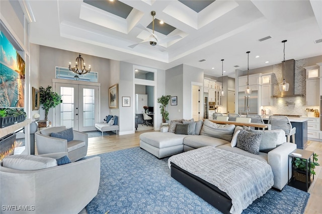 living room featuring a towering ceiling, coffered ceiling, ceiling fan with notable chandelier, wood-type flooring, and beam ceiling