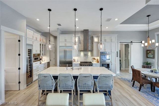 kitchen with pendant lighting, wall chimney exhaust hood, a barn door, a large island, and stainless steel appliances