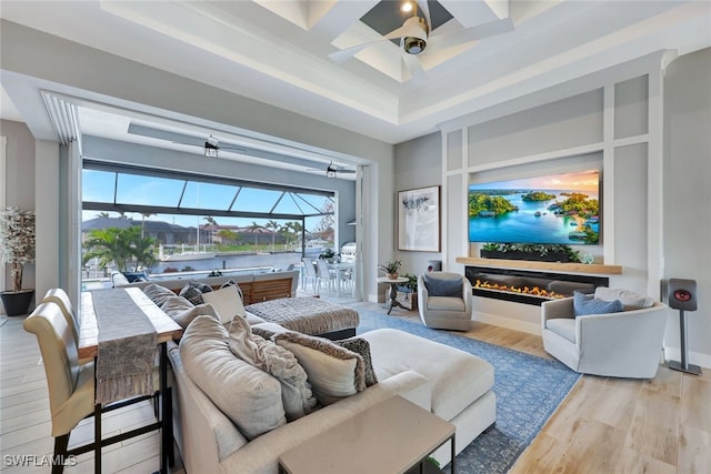 living room with wood-type flooring, a water view, a raised ceiling, and ceiling fan