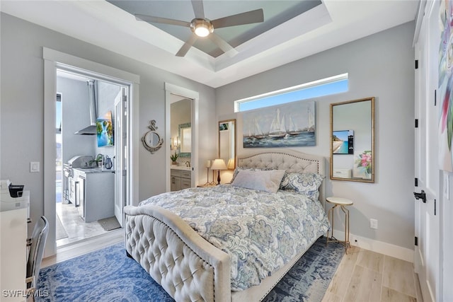 bedroom with ceiling fan, light wood-type flooring, a tray ceiling, and ensuite bath