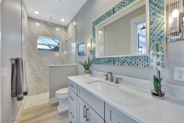 bathroom featuring hardwood / wood-style flooring, vanity, toilet, and a tile shower