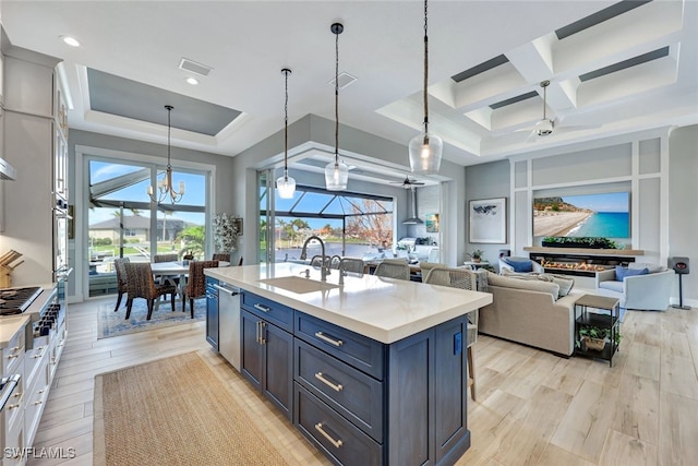 kitchen featuring light wood-type flooring, coffered ceiling, sink, decorative light fixtures, and an island with sink